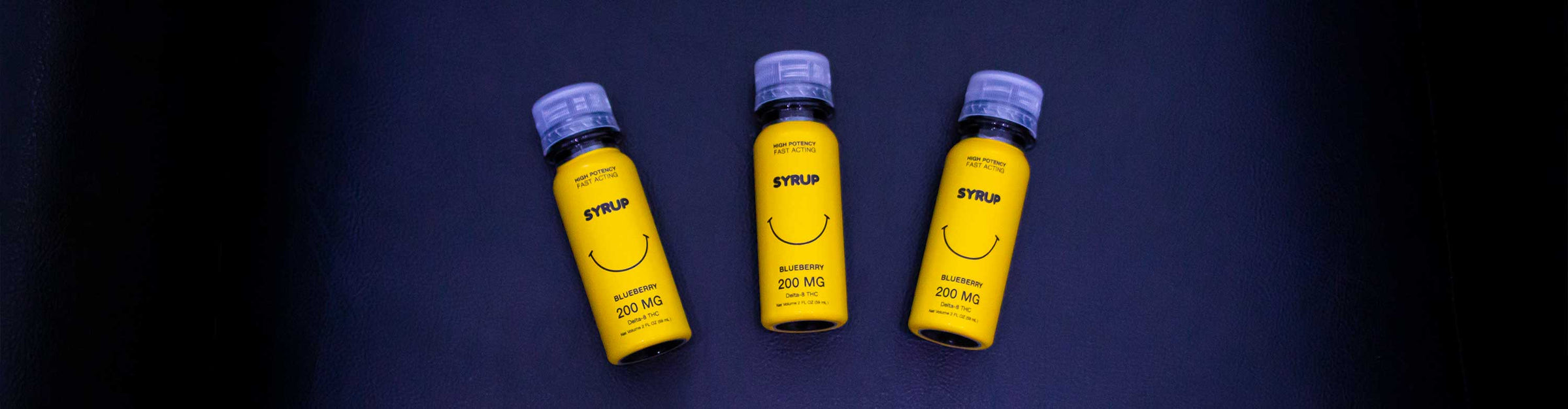 Three wholesale Sweet Life Delta 8 blueberry flavored Syrup bottles by Qwin, resting on a leather textured background with featured lighting.