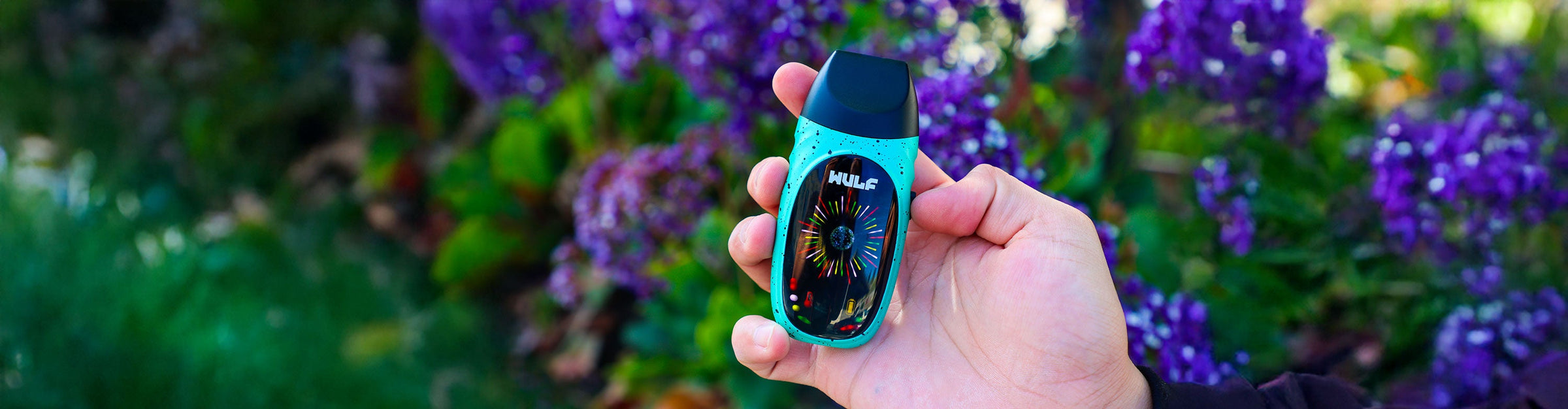 man holding the Wulf Faze Dry Herb Vaporizer with purple flowers in background