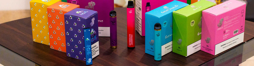 Wholesale Lush disposable vaporizers resting on a wooden countertop with several flavors including hibiscus and strawberry watermelon.