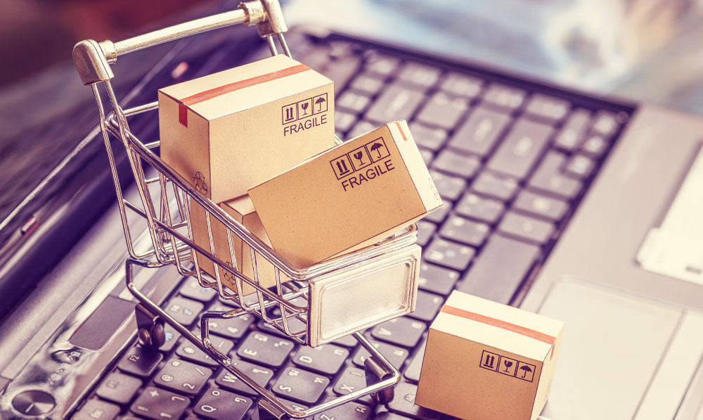 E-Commerce image of a small shopping cart with packaging resting on laptop