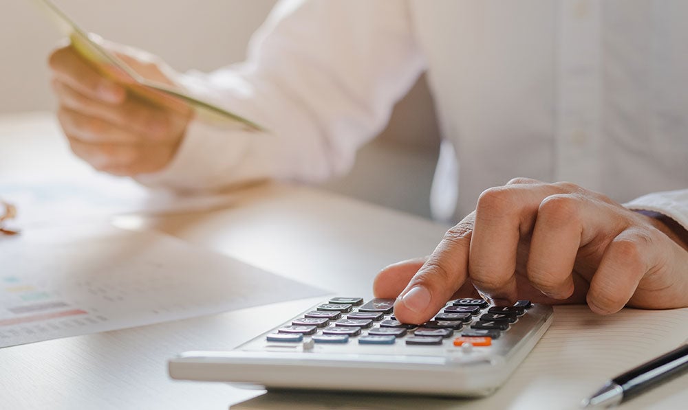 man in white shirt using calculator checking investments