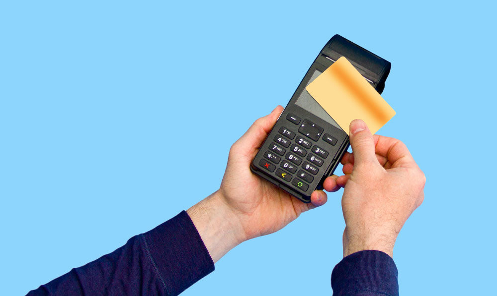 Hand holding credit card processor over blue studio background