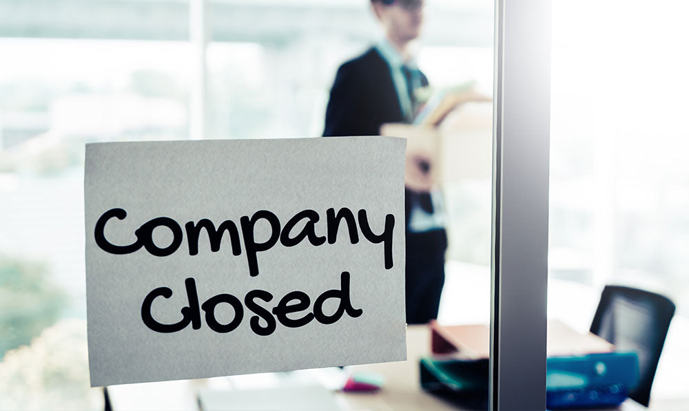posted note saying company closed with business man packing up his office supplies