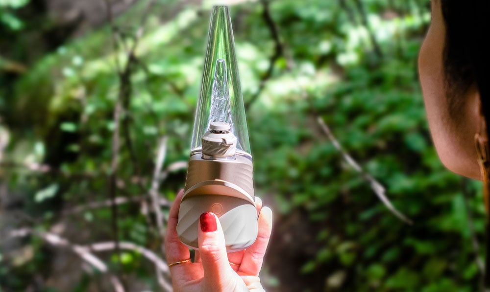 Woman holding Puffco New Peak Pro Desert in front of park trail