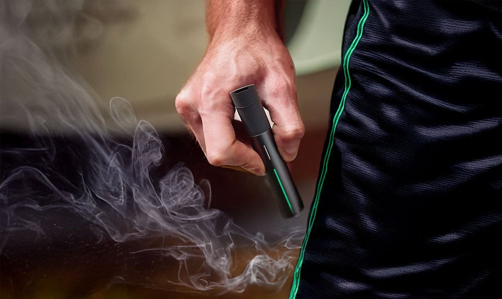 Man in soccer shorts holding Puffco Pivot with smoke nearby
