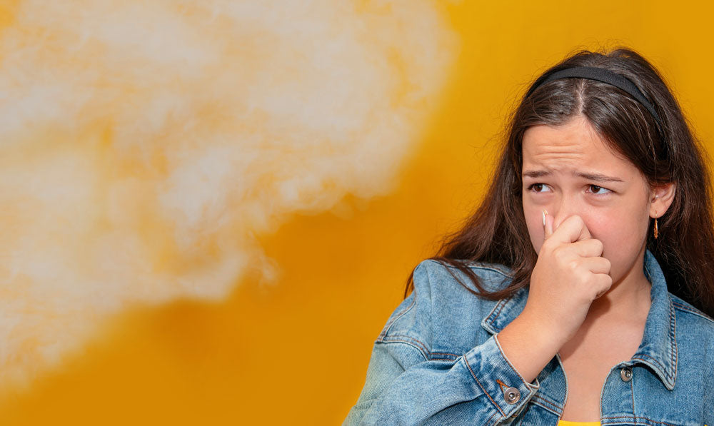 Woman smelling smoke in front of orange background