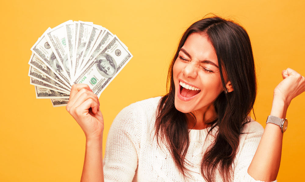 Smiling woman holding cash in front of orange background