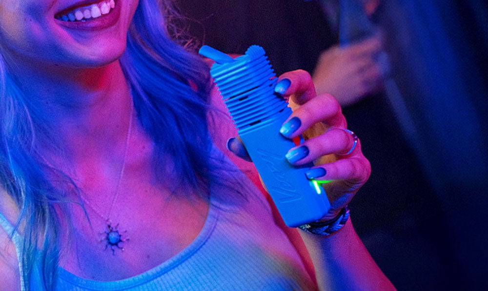 Woman with blue nails holding Storz & Bickel Veazy in dark party environment