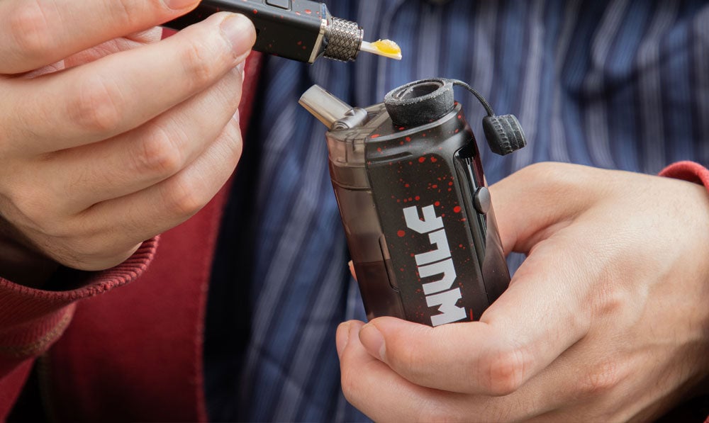 man in red jacket blue shirt holding Wulf Growler mod vape and putting wax into it from top