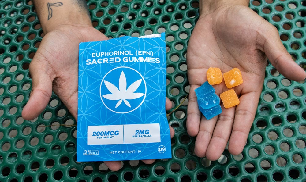 man holding Sacred EPN gummies in both hands with the packaging on the other hands showcasing the product on a lunch style table