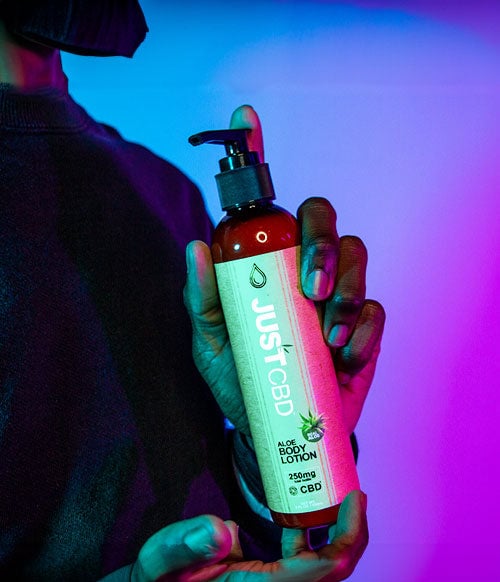 Just CBD Lotion in man's hand in front of purple and blue studio background