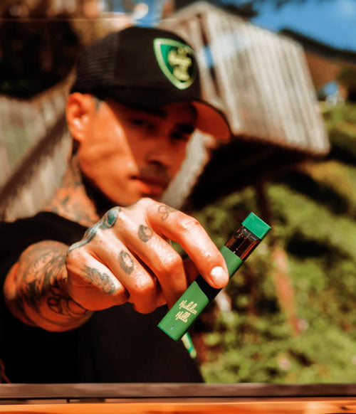 Man with tattoos holding Hidden Hills disposable