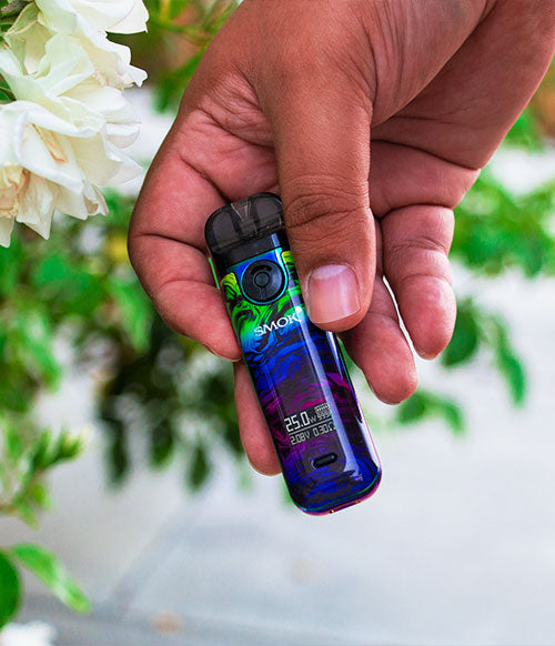 man holding SMOK Novo 4 near flowers