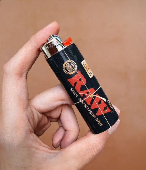 man holding RAW BIC lighter on brown background
