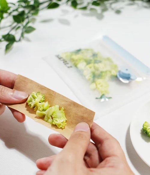 woman wrapping broccoli with sealz bag in background