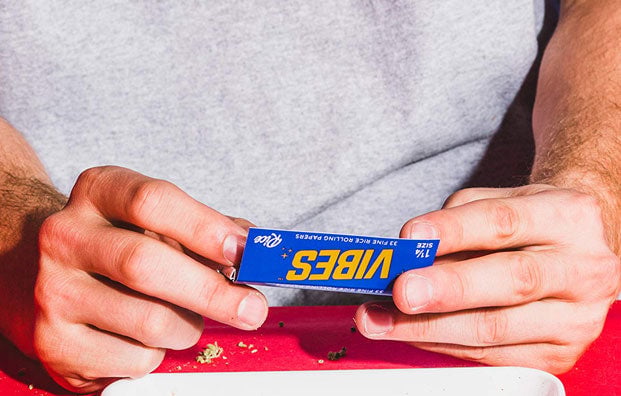 Person rolling vibes paper on top of red surface