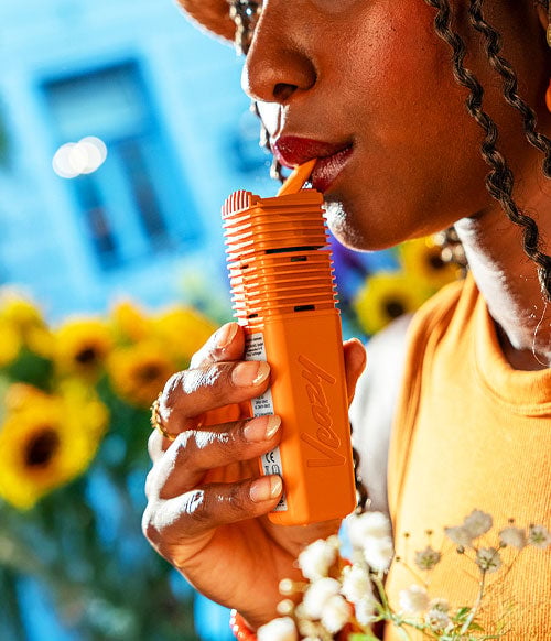 Woman holding Orange Storz & Bickel Veazy near sunflowers